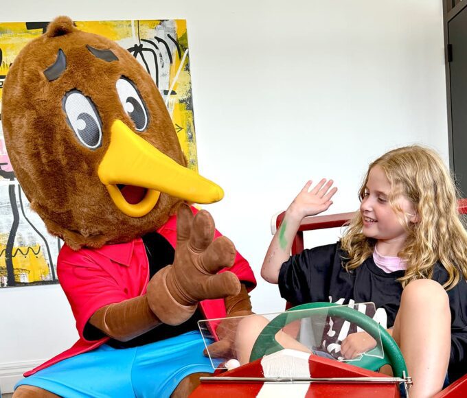 Milly, a young girl, stars in a Kiwi Mobile advertisement, pictured with Kiwi the mascot, sitting in a toy car used in the film shoot.